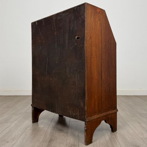 fig 6. An Edwardian oak bureau featuring a slanted fall-front lid above three drawers with decorative circular brass drop handles.