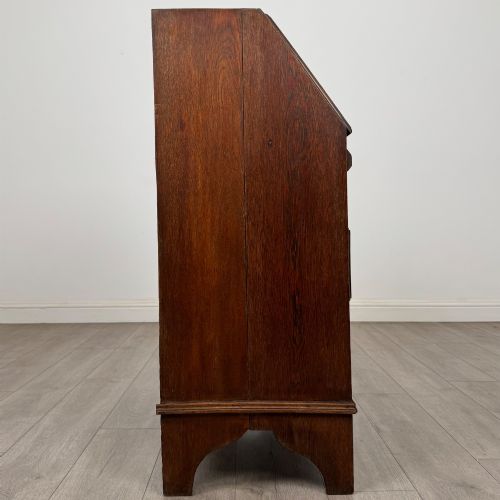 fig 7. An Edwardian oak bureau featuring a slanted fall-front lid above three drawers with decorative circular brass drop handles.