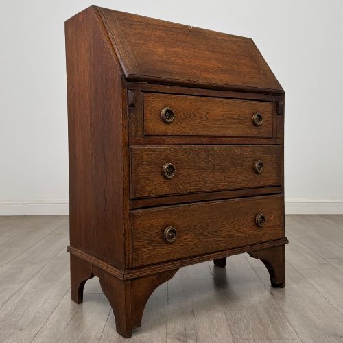 fig 8. An Edwardian oak bureau featuring a slanted fall-front lid above three drawers with decorative circular brass drop handles.