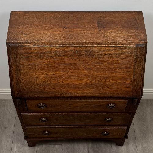 fig 9. An Edwardian oak bureau featuring a slanted fall-front lid above three drawers with decorative circular brass drop handles.