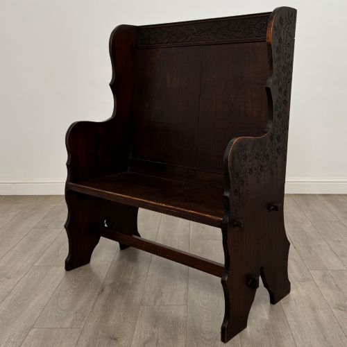 fig 1. A dark oak high-back settle featuring a floral relief carving along the top rail, shaped side panels, and a stretcher base.