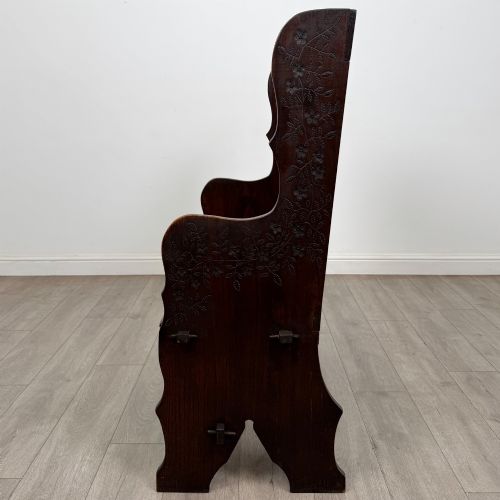 fig 2. A dark oak high-back settle featuring a floral relief carving along the top rail, shaped side panels, and a stretcher base.
