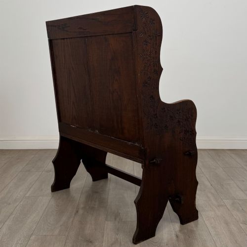 fig 5. A dark oak high-back settle featuring a floral relief carving along the top rail, shaped side panels, and a stretcher base.