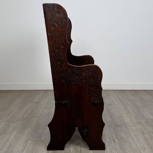 fig 6. A dark oak high-back settle featuring a floral relief carving along the top rail, shaped side panels, and a stretcher base.