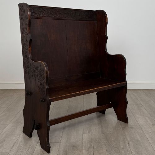 fig 7. A dark oak high-back settle featuring a floral relief carving along the top rail, shaped side panels, and a stretcher base.