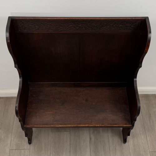 fig 8. A dark oak high-back settle featuring a floral relief carving along the top rail, shaped side panels, and a stretcher base.
