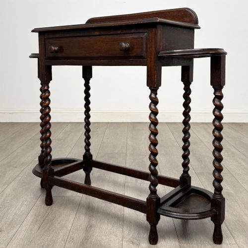 fig 1. A dark oak Edwardian hall stand featuring turned barley twist legs, a central drawer with wooden knobs, and built-in side umbrella holders with drip trays.