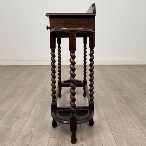 fig 2. A dark oak Edwardian hall stand featuring turned barley twist legs, a central drawer with wooden knobs, and built-in side umbrella holders with drip trays.