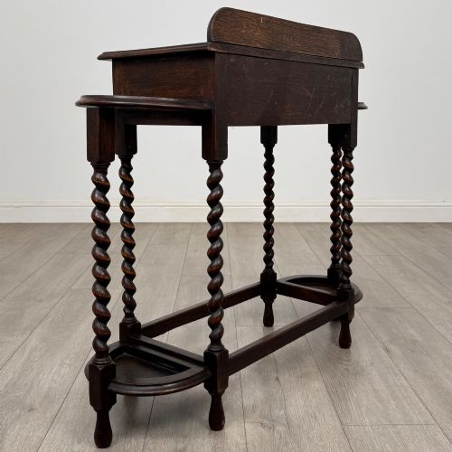 fig 3. A dark oak Edwardian hall stand featuring turned barley twist legs, a central drawer with wooden knobs, and built-in side umbrella holders with drip trays.