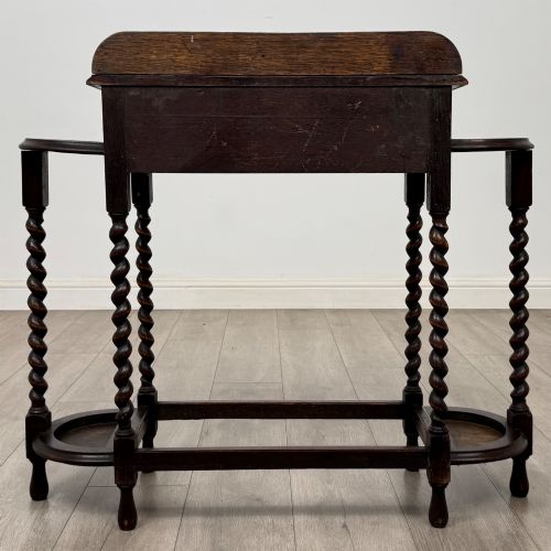 fig 4. A dark oak Edwardian hall stand featuring turned barley twist legs, a central drawer with wooden knobs, and built-in side umbrella holders with drip trays.