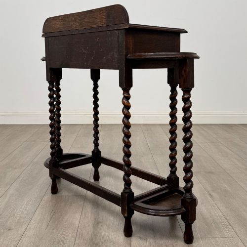 fig 5. A dark oak Edwardian hall stand featuring turned barley twist legs, a central drawer with wooden knobs, and built-in side umbrella holders with drip trays.