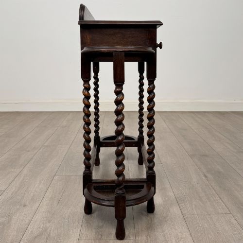 fig 6. A dark oak Edwardian hall stand featuring turned barley twist legs, a central drawer with wooden knobs, and built-in side umbrella holders with drip trays.