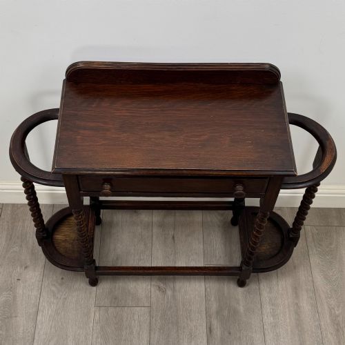fig 8. A dark oak Edwardian hall stand featuring turned barley twist legs, a central drawer with wooden knobs, and built-in side umbrella holders with drip trays.