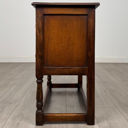 fig 3. A small warm brown carved oak cupboard with double doors featuring carved arches, iron hinges, turned legs, and a lower stretcher base.