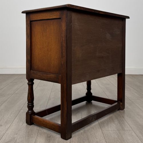 fig 4. A small warm brown carved oak cupboard with double doors featuring carved arches, iron hinges, turned legs, and a lower stretcher base.