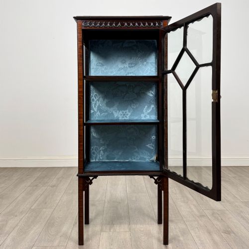 fig 1. A slender Edwardian mahogany glazed display cabinet featuring astragal door bars and a fabric-lined interior raised on square legs.