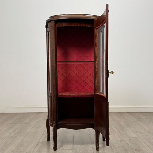 fig 1. A French mahogany display vitrine featuring a curved glass door, red fabric interior lining, floral marquetry lower panel, and brass leg mounts.
