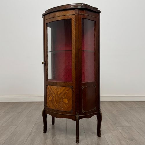 fig 2. A French mahogany display vitrine featuring a curved glass door, red fabric interior lining, floral marquetry lower panel, and brass leg mounts.