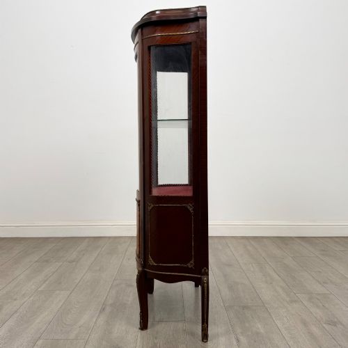 fig 3. A French mahogany display vitrine featuring a curved glass door, red fabric interior lining, floral marquetry lower panel, and brass leg mounts.