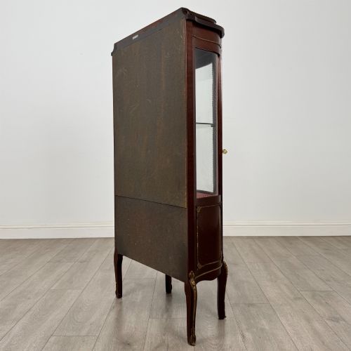 fig 6. A French mahogany display vitrine featuring a curved glass door, red fabric interior lining, floral marquetry lower panel, and brass leg mounts.