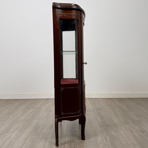 fig 7. A French mahogany display vitrine featuring a curved glass door, red fabric interior lining, floral marquetry lower panel, and brass leg mounts.