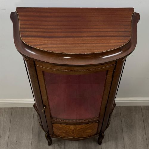fig 9. A French mahogany display vitrine featuring a curved glass door, red fabric interior lining, floral marquetry lower panel, and brass leg mounts.