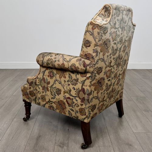 fig 2. A 19th-century wingback armchair upholstered in floral tapestry fabric with turned mahogany front legs on brass castors.