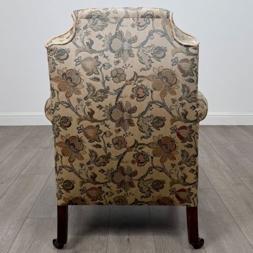 fig 3. A 19th-century wingback armchair upholstered in floral tapestry fabric with turned mahogany front legs on brass castors.