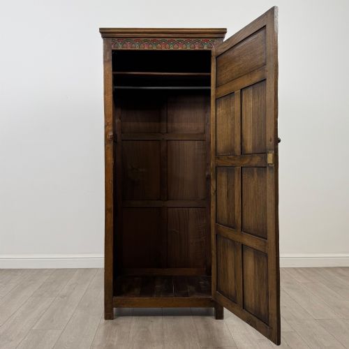 fig 1. A narrow twentieth-century dark oak single-door wardrobe featuring carved scrollwork panels, a decorative painted top frieze, and panelled construction.