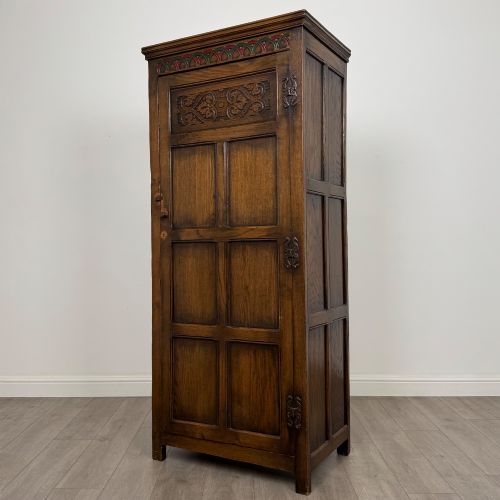 fig 2. A narrow twentieth-century dark oak single-door wardrobe featuring carved scrollwork panels, a decorative painted top frieze, and panelled construction.
