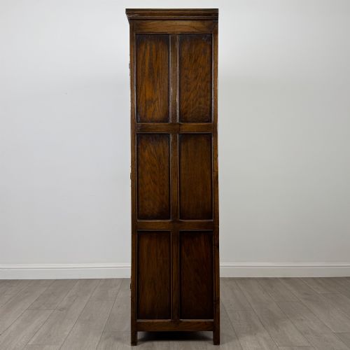 fig 3. A narrow twentieth-century dark oak single-door wardrobe featuring carved scrollwork panels, a decorative painted top frieze, and panelled construction.