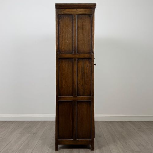 fig 7. A narrow twentieth-century dark oak single-door wardrobe featuring carved scrollwork panels, a decorative painted top frieze, and panelled construction.