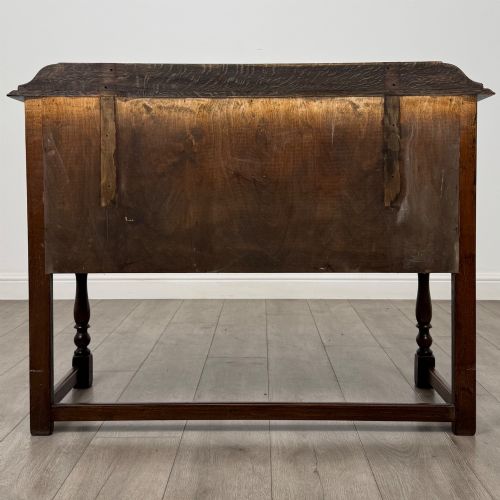 fig 4. A dark oak chest featuring two top drawers above one wide bottom drawer, resting on turned legs connected by a low stretcher frame.