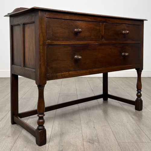 fig 7. A dark oak chest featuring two top drawers above one wide bottom drawer, resting on turned legs connected by a low stretcher frame.