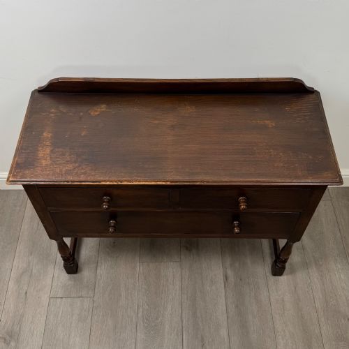 fig 8. A dark oak chest featuring two top drawers above one wide bottom drawer, resting on turned legs connected by a low stretcher frame.