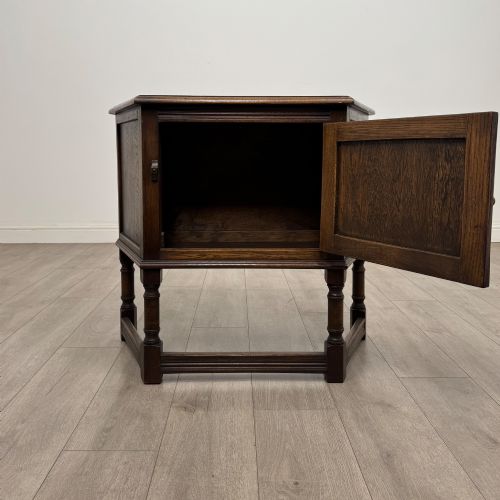 fig 1. A small dark oak cupboard featuring a single carved panel door, turned legs, a lower stretcher, and decorative brass hinges.