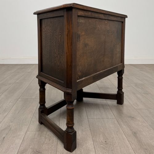 fig 4. A small dark oak cupboard featuring a single carved panel door, turned legs, a lower stretcher, and decorative brass hinges.