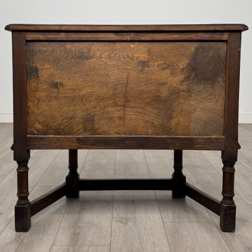 fig 5. A small dark oak cupboard featuring a single carved panel door, turned legs, a lower stretcher, and decorative brass hinges.