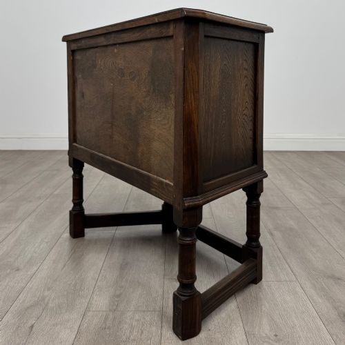 fig 6. A small dark oak cupboard featuring a single carved panel door, turned legs, a lower stretcher, and decorative brass hinges.