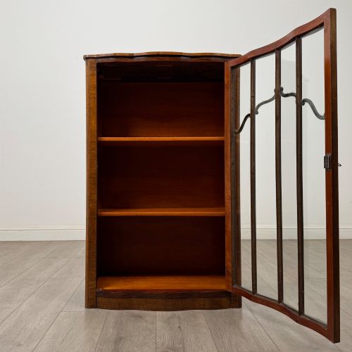 fig 1. A freestanding early 20th-century display cabinet featuring figured walnut veneers, a single glazed door with decorative astragal glazing bars, and internal wooden shelves.