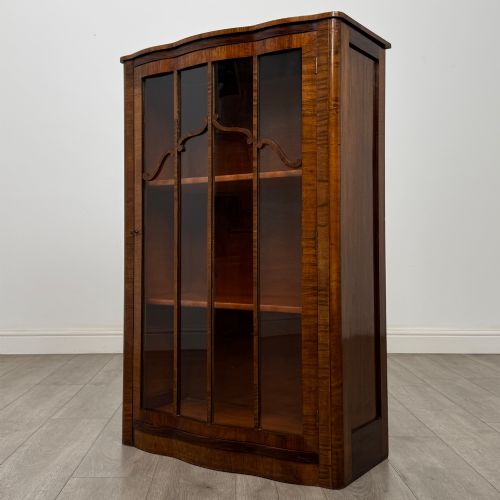 fig 2. A freestanding early 20th-century display cabinet featuring figured walnut veneers, a single glazed door with decorative astragal glazing bars, and internal wooden shelves.