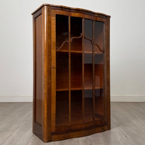 fig 8. A freestanding early 20th-century display cabinet featuring figured walnut veneers, a single glazed door with decorative astragal glazing bars, and internal wooden shelves.