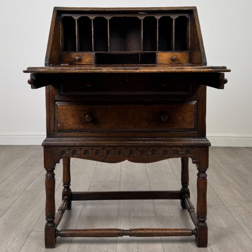 fig 1. A dark oak antique bureau featuring a slanted drop-front lid above two drawers, supported by turned legs and stretchers.