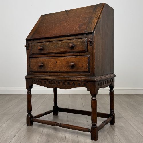 fig 2. A dark oak antique bureau featuring a slanted drop-front lid above two drawers, supported by turned legs and stretchers.