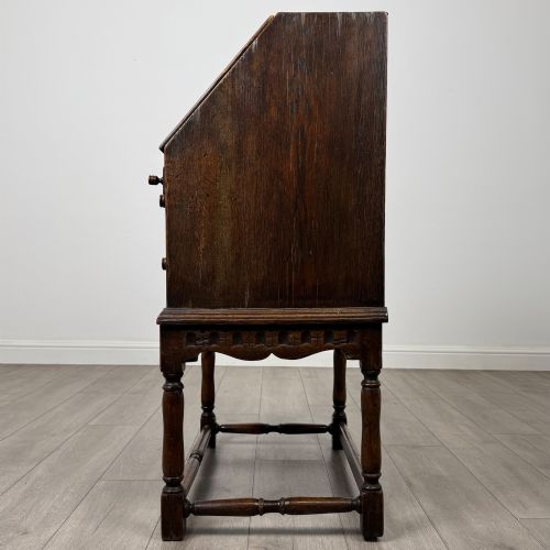 fig 3. A dark oak antique bureau featuring a slanted drop-front lid above two drawers, supported by turned legs and stretchers.