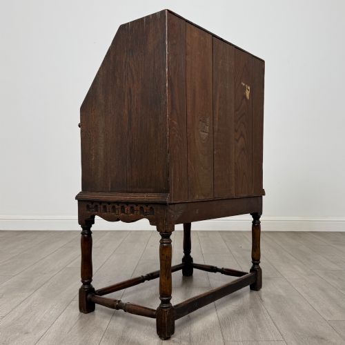 fig 4. A dark oak antique bureau featuring a slanted drop-front lid above two drawers, supported by turned legs and stretchers.