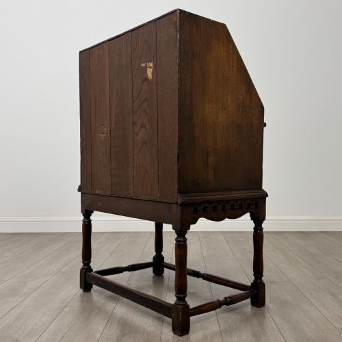 fig 6. A dark oak antique bureau featuring a slanted drop-front lid above two drawers, supported by turned legs and stretchers.