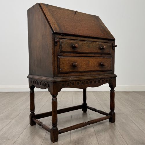 fig 8. A dark oak antique bureau featuring a slanted drop-front lid above two drawers, supported by turned legs and stretchers.