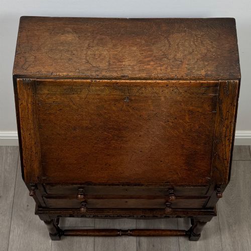 fig 9. A dark oak antique bureau featuring a slanted drop-front lid above two drawers, supported by turned legs and stretchers.