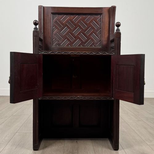 fig 1. A dark mahogany hall seat cabinet featuring a carved geometric back panel, decorative brass strap hinges, double cupboard doors, and finial corner posts.